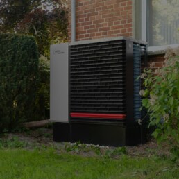 Außeneinheit einer Wärmepumpe vor einem sanierten Backsteinhaus